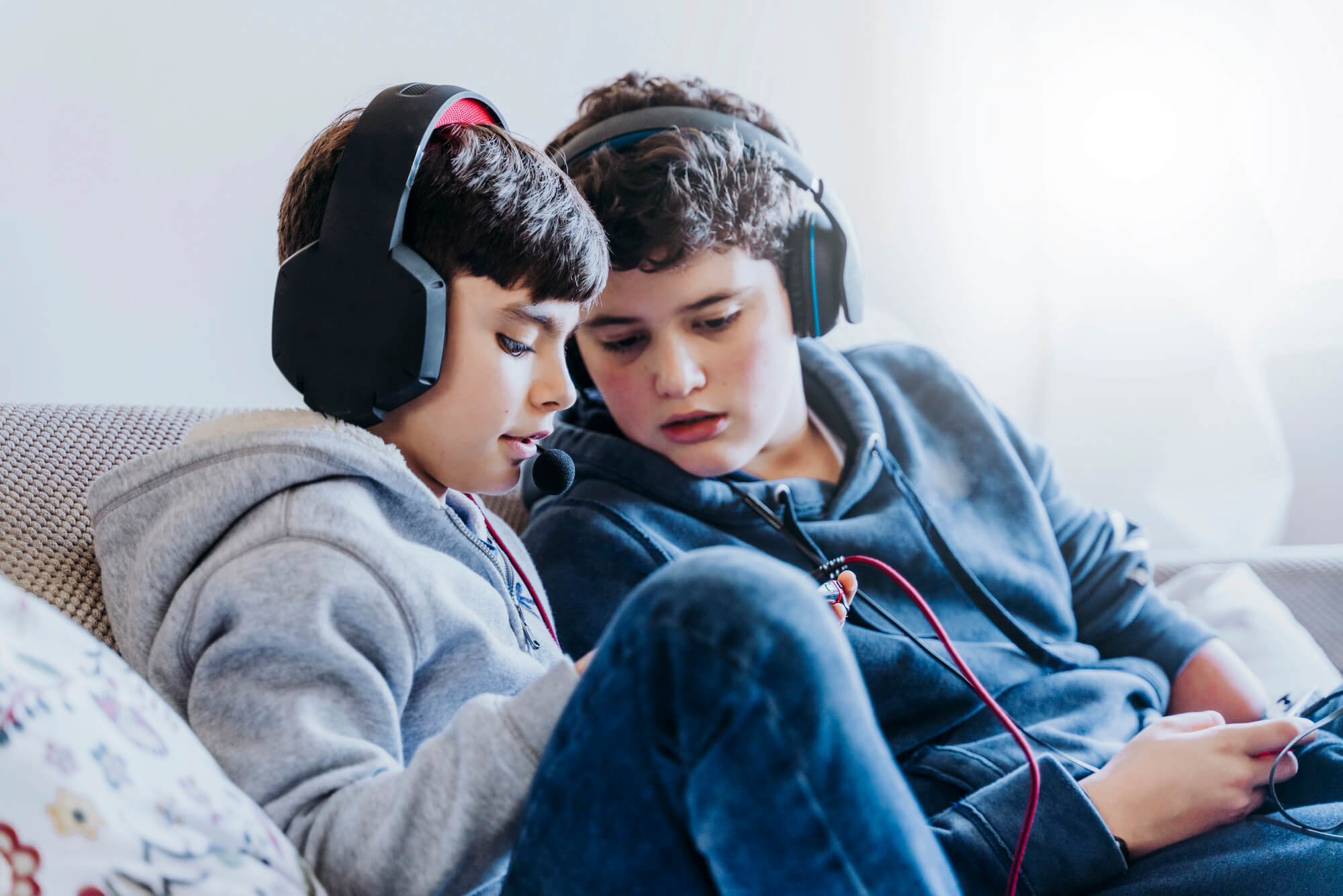 Two kids lying on couch and playing with a video game console at home